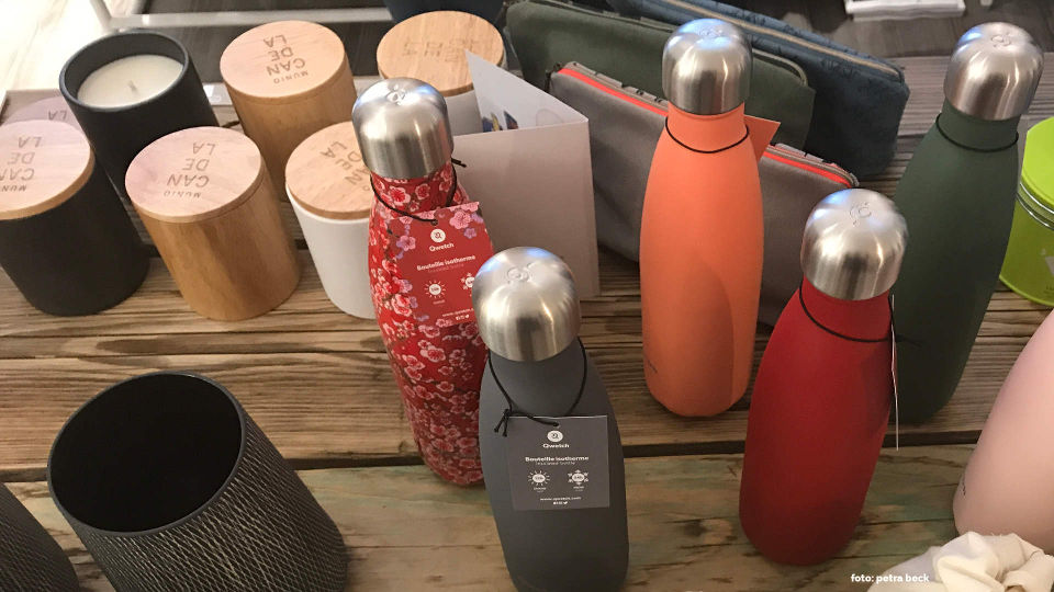 6 bunte Edelstahlflaschen auf einem Holztisch, im Hintergrund weitere plastikfreie Produkte