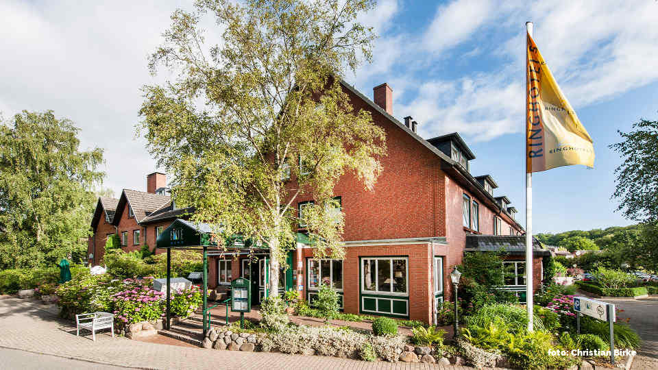 Ansicht des weitgehend plastikfrei bewirtschafteten Hotel Birke in Kiel an einem schönen Sommertag mit Bäumen und Rosenbusch.