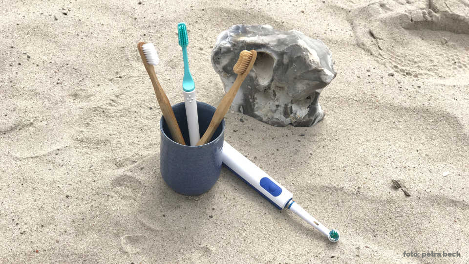 Vier Zahnbürsten im Becher am Strand.