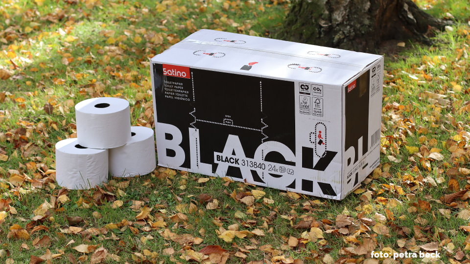 Ein Karton des Toilettenpapiers von Satino Black auf einem Rasen mit buntem Herbstlaub