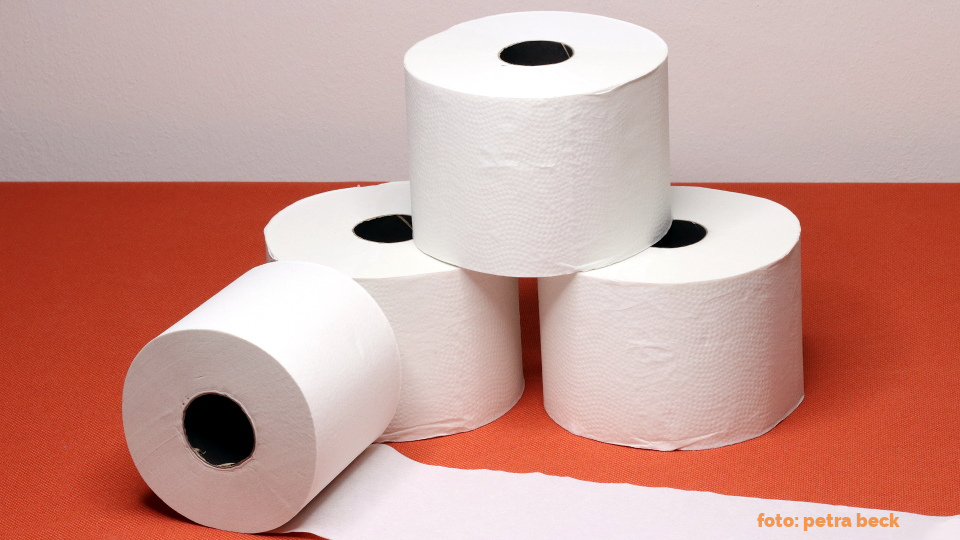 Drei Toilettenpapierrollen als Turm und eine aufgerollte Rolle auf oranger Tischdecke