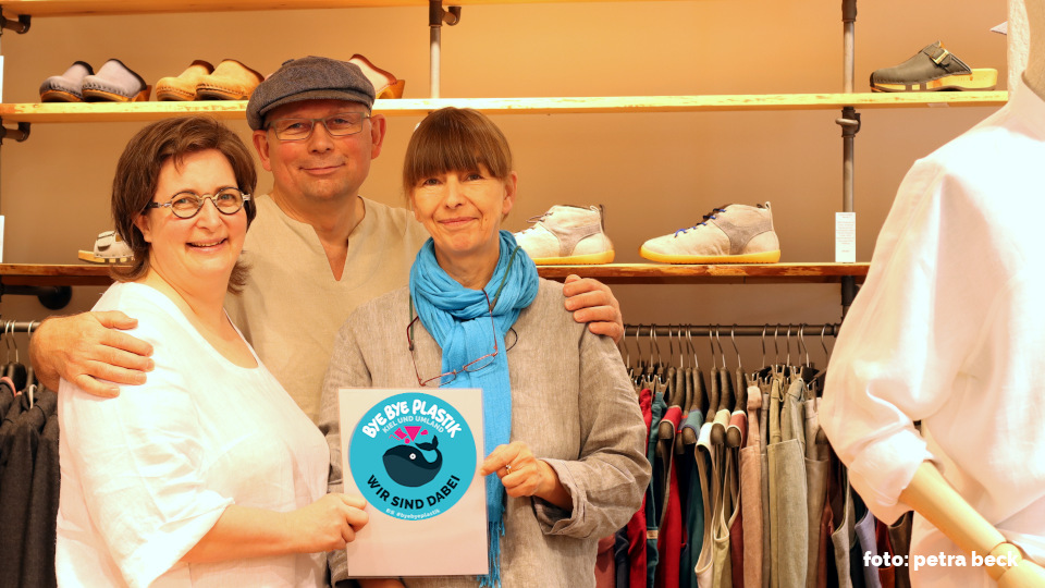 Nathalie und Josef Skultety mit ihrer Mitarbeiterin Heike stehen vor einem Kleiderregal auf dem Schuhe stehen und Kleidung hängt.