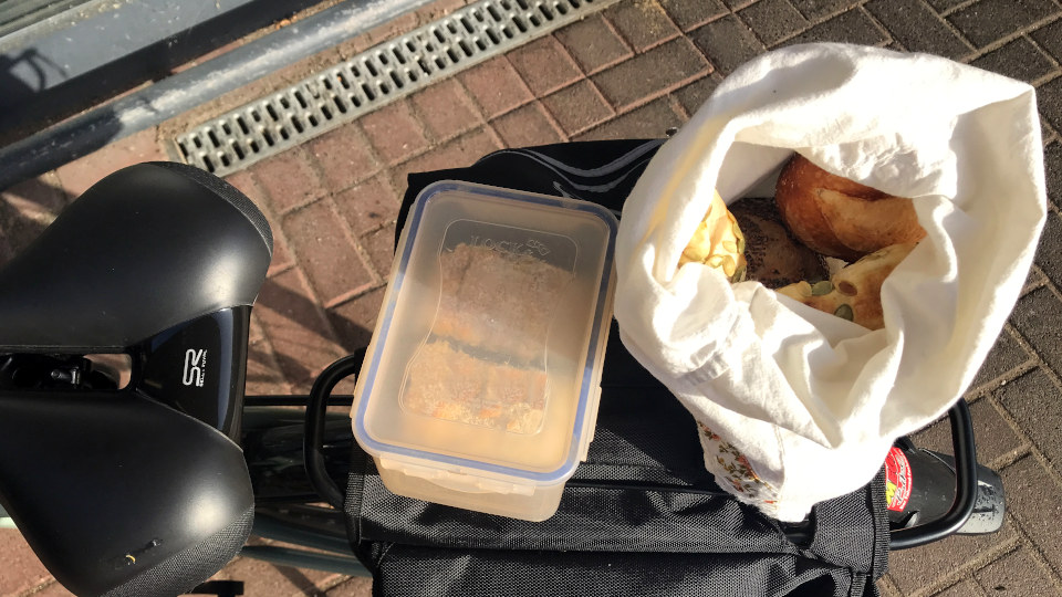 Einkäufe mit eigenen Behältern - auf einem Fahrrad steht ein Behälter mit Kuchen und ein Stoffbeutel, in dem sich Brötchen befinden.