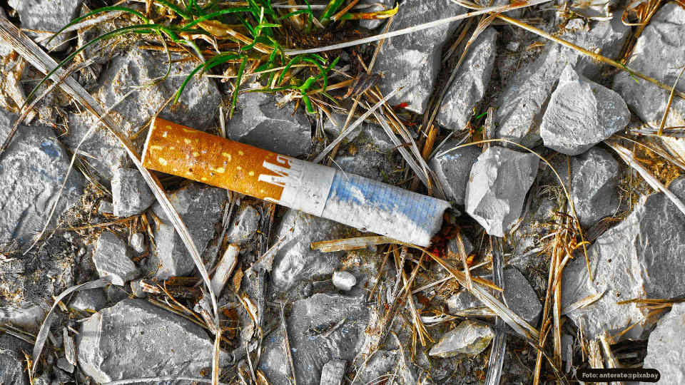 Zigarettenkippe auf dem Boden zwischen Steinen liegend