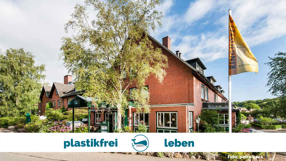 Vorderansicht des weitgehend plastikfrei bewirtschafteten Hotel Birke in Kiel an einem schönen Sommertag mit Bäumen und Fahnenmast.