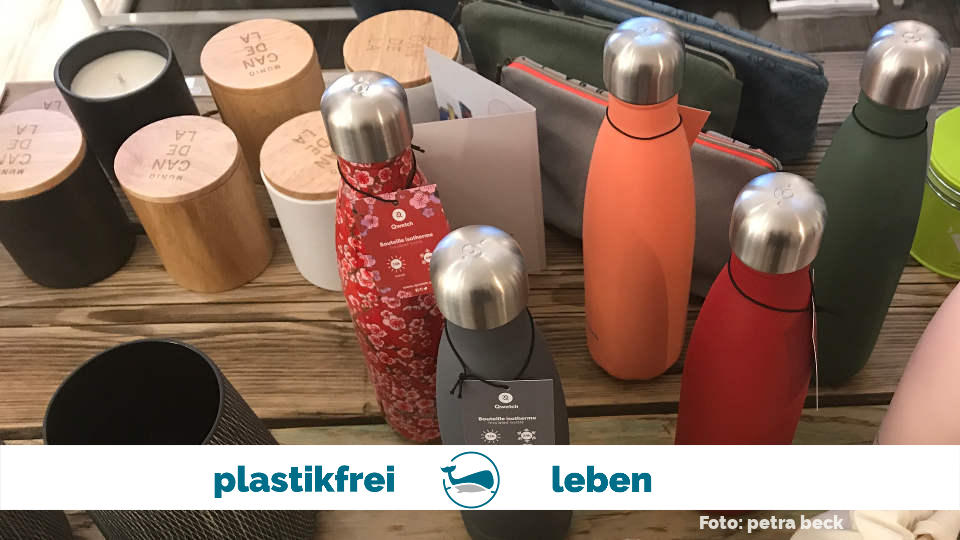 6 bunte Edelstahlflaschen auf einem Holztisch, im Hintergrund weitere plastikfreie Produkte